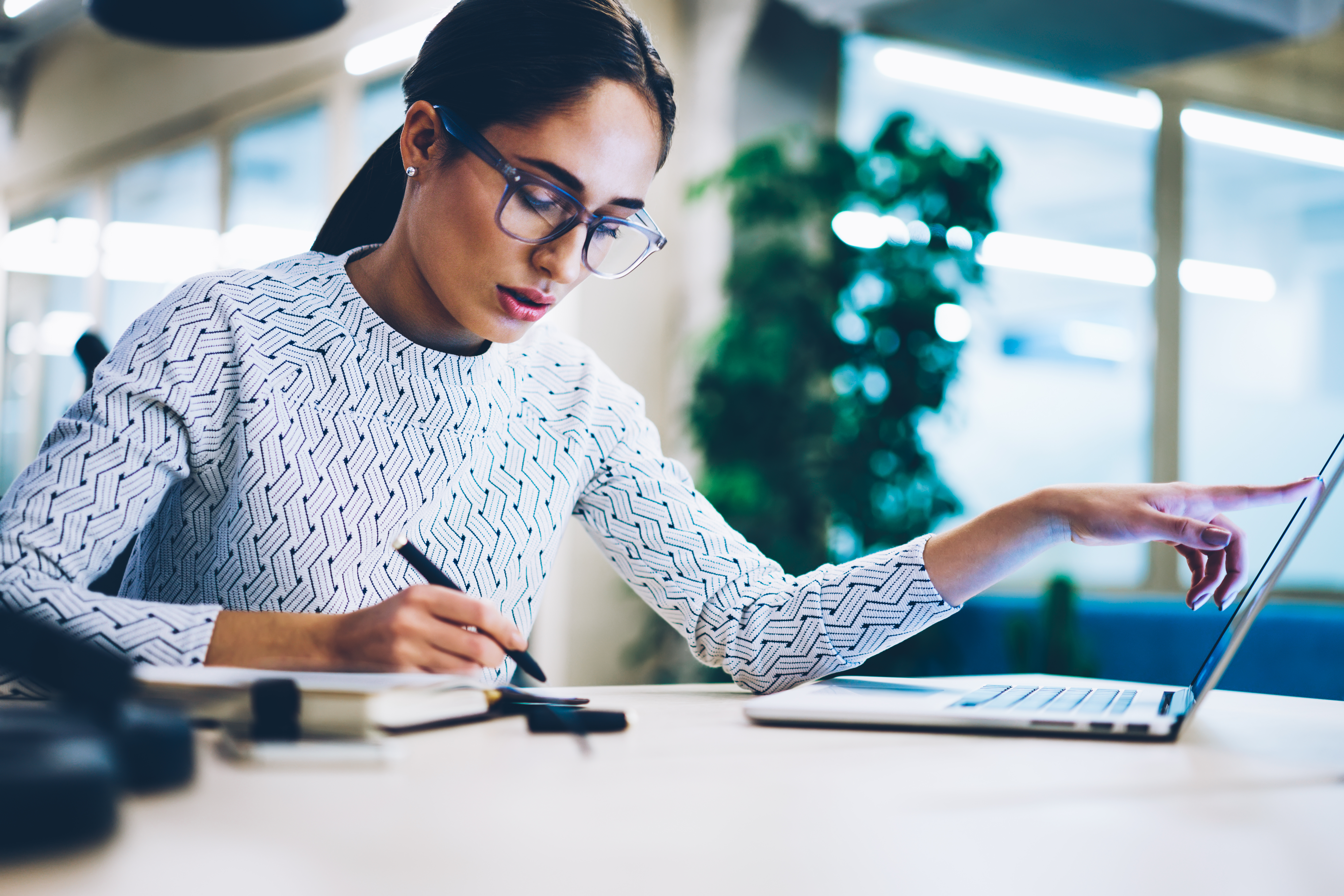 woman writing something on paper and pointing to her computer