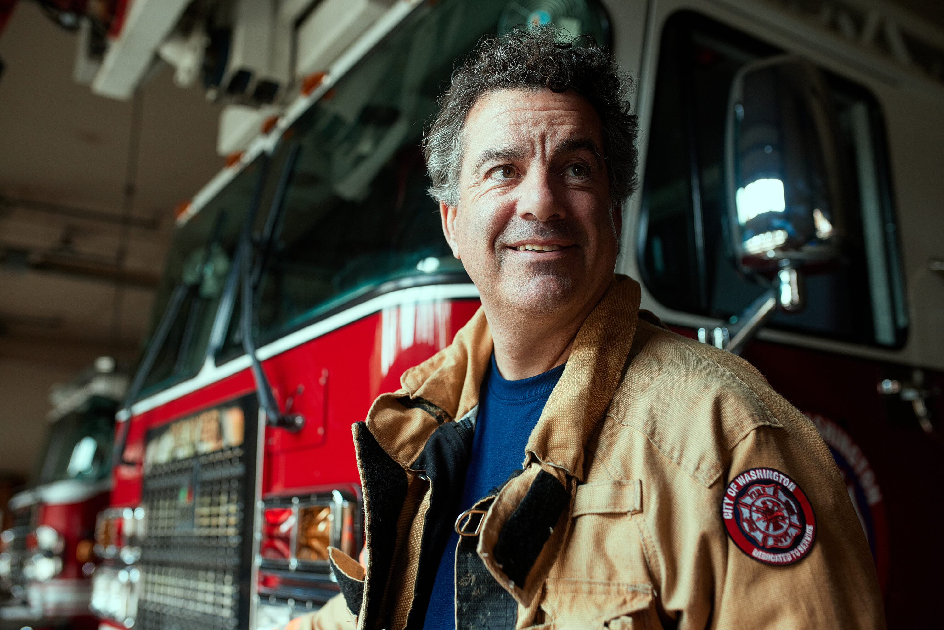 Firefighter smiling in front of a firetruck in a fire station.
