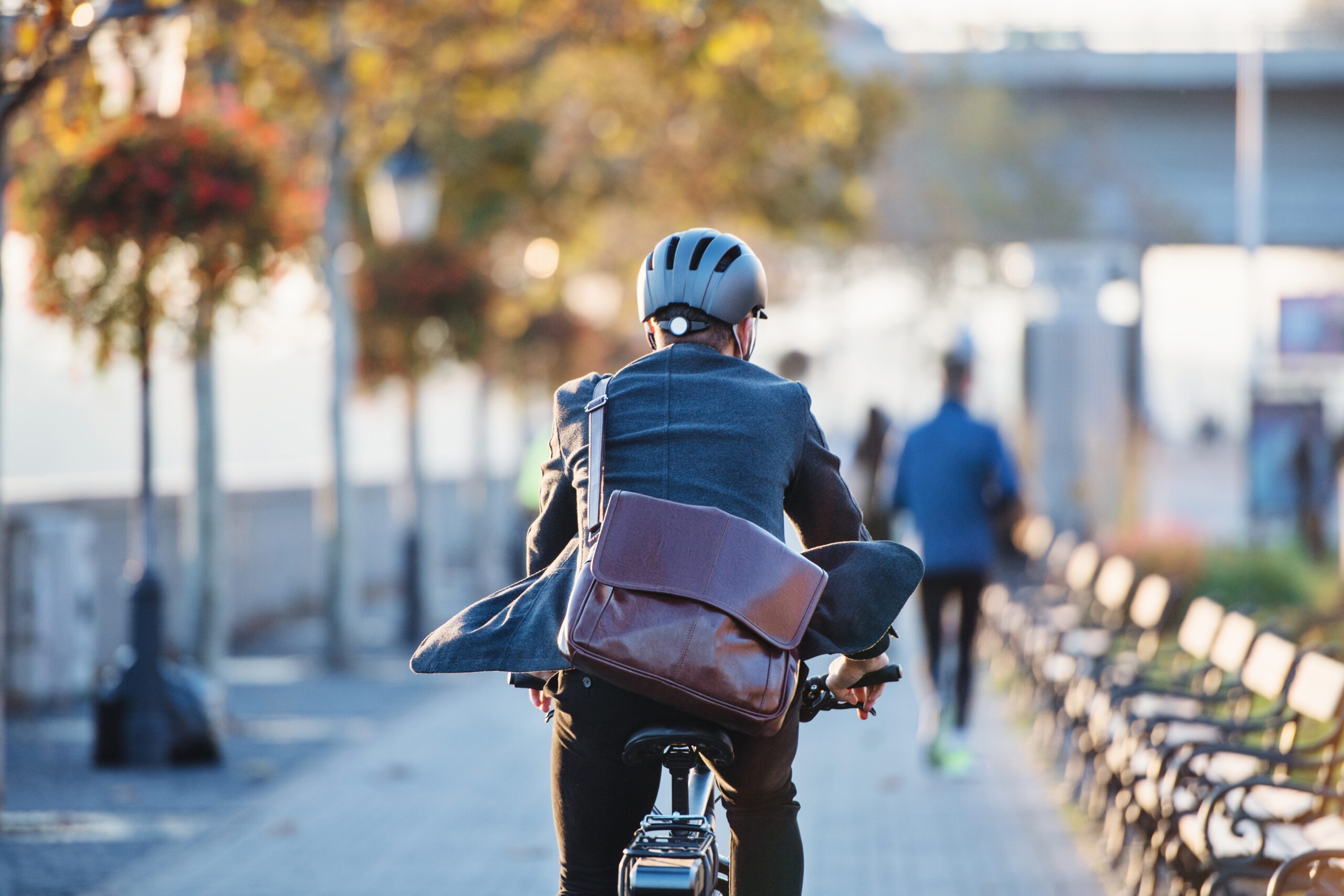 A rear view of businessman commuter with electric bicycle traveling to work in city.