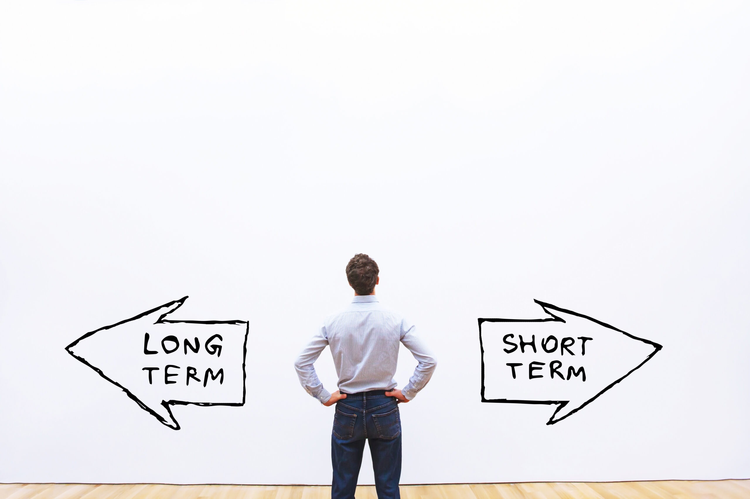 Man standing in front of two arrows. One that says short term and one that says long term.