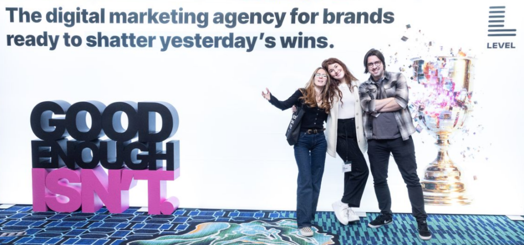 Level Agency and BAM Strategy team members posing with the "Good Enough Isn't" sign at the All In Summit