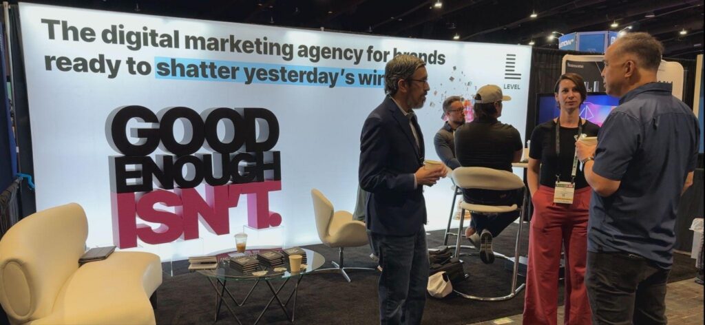 Attendees in conversation at the Level Agency booth at LeadsCon 2026 in front of the Good Enough Isn't backdrop
