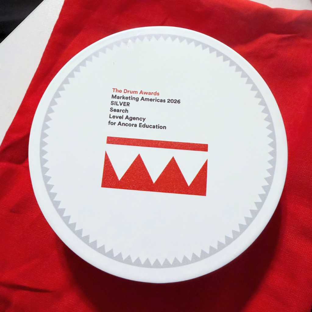 Level Agency's circular white The Drum Awards trophy resting on red fabric, engraved with "The Drum Awards Marketing Americas 2026, SILVER, Search, Level Agency for Ancora Education" above the red Drum crown logo.