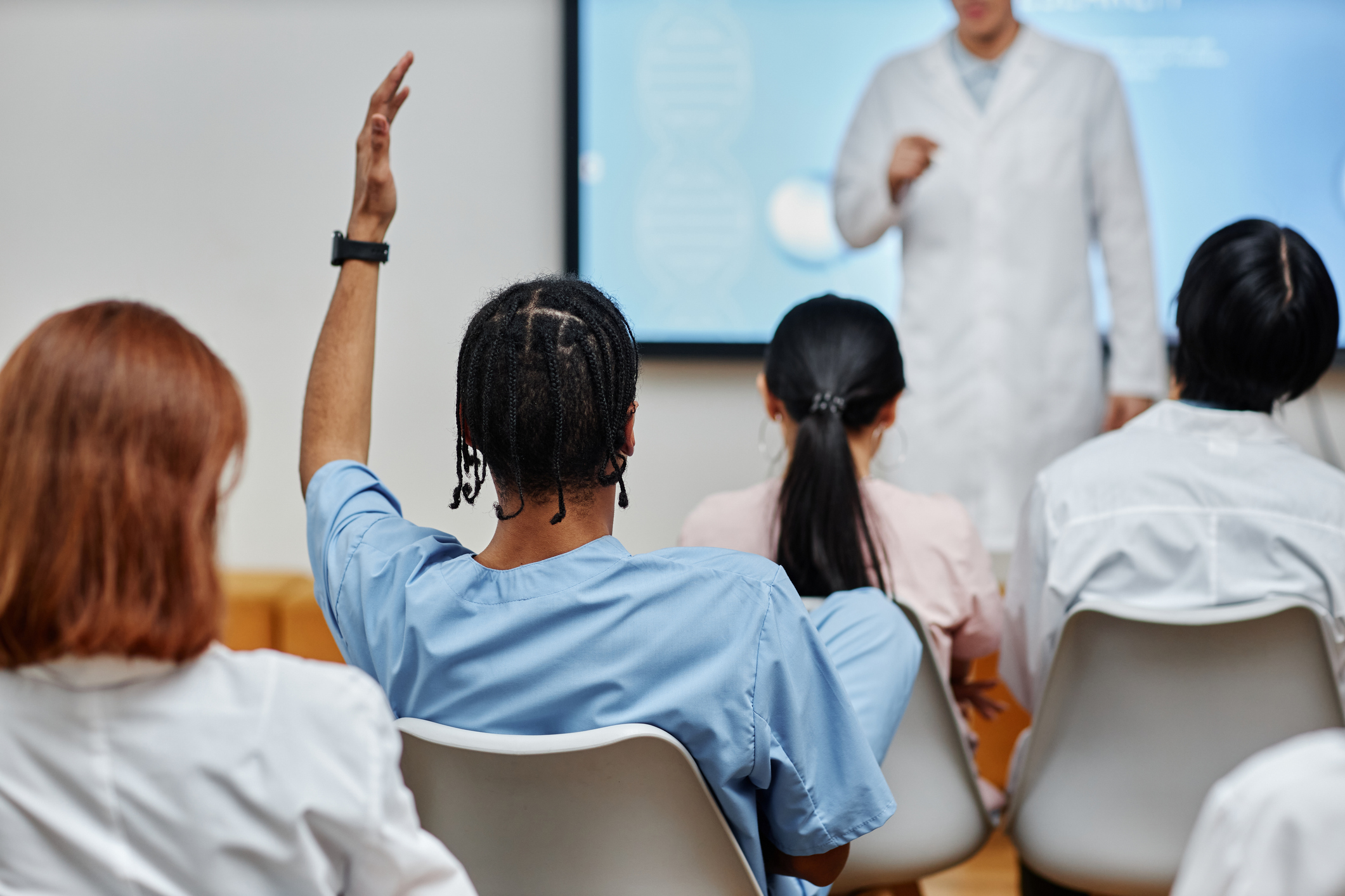 Nursing student raising a hand during a health sciences lecture, the inquiry stage that offline conversions link to enrollment